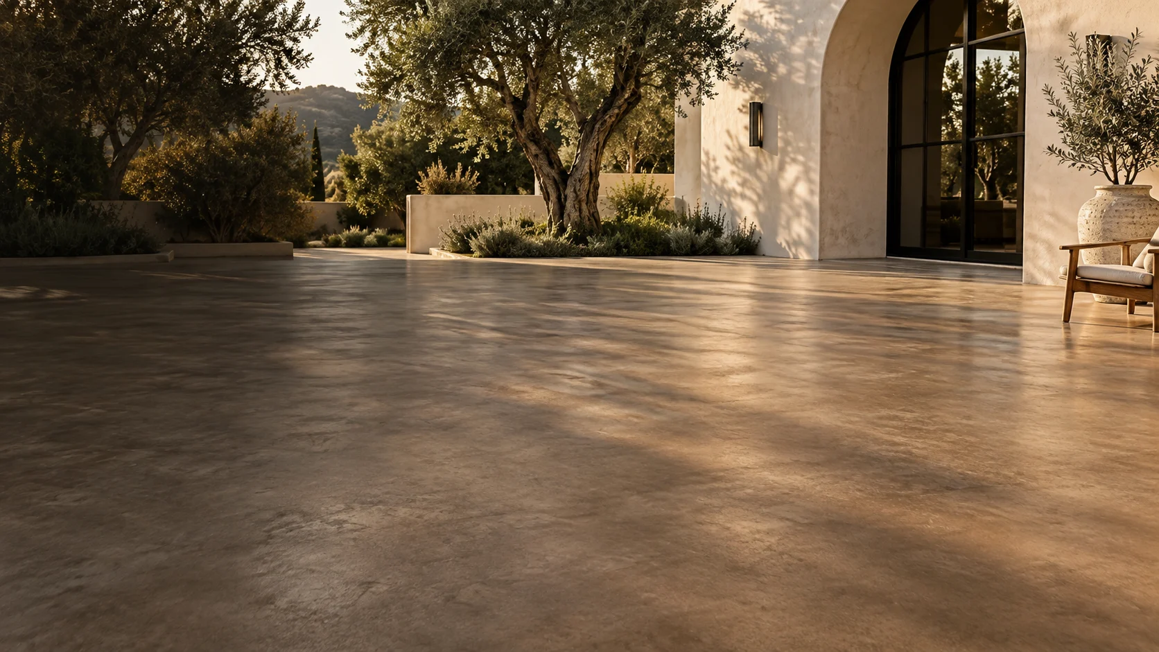 Illustrative sunlit courtyard with richly textured stained concrete, olive trees and warm plaster architecture